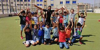 Gruppenbild einer Sportgruppe mit Trainer/Sportlehrkraft auf dem Sportplatz vor Schulgebäude