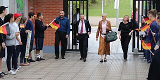 Schülerinnen und Schüler bilden ein Spalier für Generalkonsul und Fachberatung und schwenken kleine deutsche Flaggen