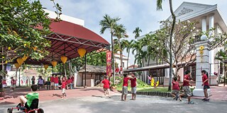 Gebäude von außen mit spielenden Schulkindern und einem bunten Pavillon