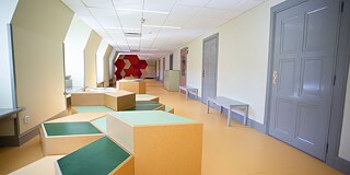 Gang in der Schule mit großer Tür und bunten Sitzgelegenheiten