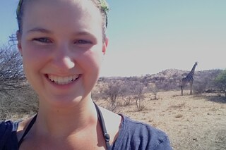 Eine Frau macht ein Selfie und lacht, im Hintergrund eine Giraffe