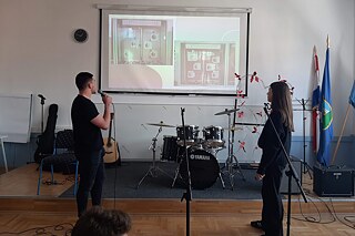 Zwei Personen mit Mikrophonen in der Hand stehen vor einem Whiteboard.