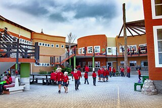 Schule mit Vorplatz, Schülerschar in rot-schwarzen Uniformen