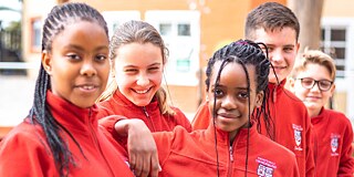 Fünf lächelnde Schülerinnen und Schüler in roter Uniform