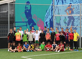 Schülerinnen und Schüler in Fußballkleidung auf einem Spielfeld. Der Mauern im Hintergrund sind bunt gestaltet.