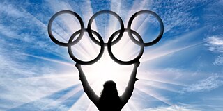 Die Siluette einer Athletin (von hinten zu sehen) hält die olympischen Ringe in den Himmel.