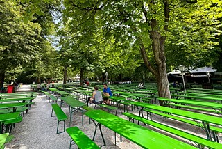 Ein Biergarten mit Bänken und Tischen unter Bäumen