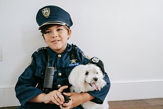 Ein kleiner Junge im Scheriffkostüm hält einen kleinen, weißen Hund in den Armen.