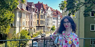 Junge Frau in einem geblümten Kleid steht auf einer Brücke. Im Hintergrund sieht man die Altstadt Göttingen.