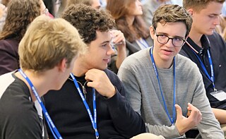 Drei junge Männer mit DAAD-Lanyards um den Hals unterhalten sich. 