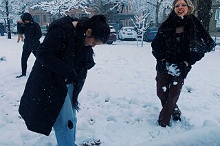 Zwei Schülerinnen in dunklen Winterjacken stehen knöcheltief im Schnee. Eine der beiden hält in ihren Händen einen geformten Schneeball.